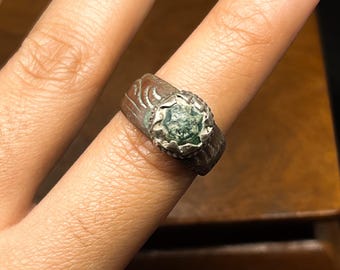 May include: A silver ring with a green stone set in a decorative silver setting. The ring has an intricate design on the band.