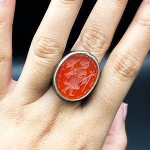 Puede incluir: Un anillo de plata con una piedra ovalada roja con un diseño grabado.