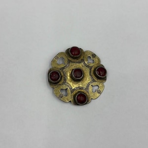 Può includere: Un fermaglio rotondo in metallo dorato con un design decorativo e cinque pietre preziose rosse.