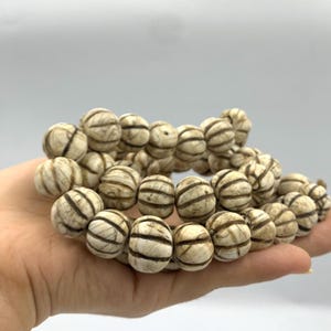 May include: A strand of white and brown striped round beads. The beads are made of bone and have a carved design.