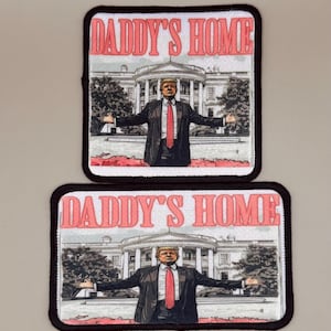 May include: Two iron-on patches with a black border and white background. The patches feature a cartoon image of a man in a suit standing in front of the White House. The text "Daddy's Home" is printed in pink letters on both patches.