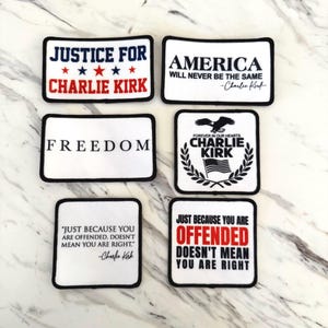 May include: Rectangular white patches with black borders. Text includes "JUSTICE FOR CHARLIE KIRK", "AMERICA WILL NEVER BE THE SAME", "FREEDOM", "FOREVER IN OUR HEARTS CHARLIE KIRK", and quotes by Charlie Kirk. Patriotic theme.