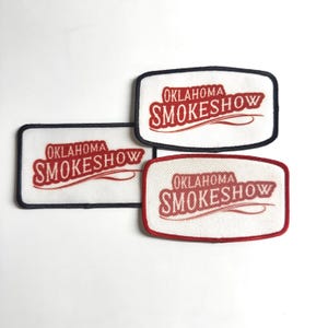 May include: Three rectangular patches with the text "OKLAHOMA SMOKESHOW" in red script on a white background. Each patch has a different colored border: black, red, and navy blue. The patches are likely for clothing or accessories.