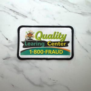 May include: A rectangular patch with a black border. The patch features the words "Quality Learning Center" in green and yellow, with a treehouse graphic. Below, it reads "1-800-FRAUD" in white text on a green and orange background.