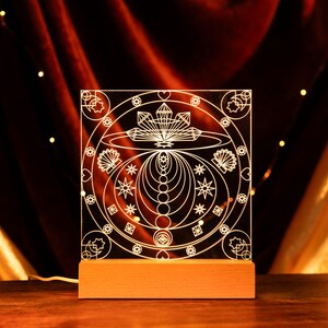 Peut inclure: Un motif géométrique blanc avec un motif circulaire est éclairé sur un panneau acrylique transparent. Le panneau est monté sur une base en bois.