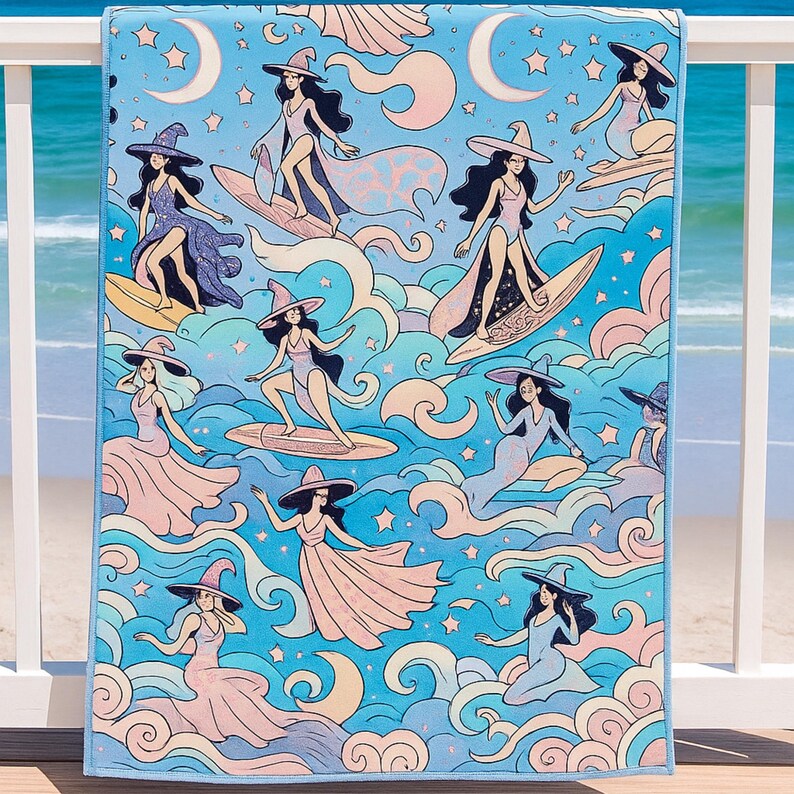A beach towel with a whimsical design features illustrated witches surfing and floating on waves. The witches wear flowing dresses and wide-brimmed hats in pastel pinks, purples, and blues. The background is filled with swirling ocean waves, crescent moons, and stars, all in soft, dreamy colors. The towel hangs over a white railing with a view of the ocean and sandy beach in the background