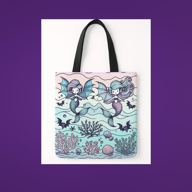 A pastel-colored tote bag features two cute mermaids with bat wings swimming in an underwater scene. Surrounded by coral, seashells, and playful bats, the background fades from soft pink to aqua. The mermaids have long flowing hair and heart details on their chests, giving a whimsical mix of spooky and sweet. The bag has black handles and is set against a purple and white backdrop