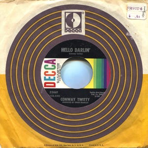 May include: Vintage 45 RPM record featuring "Hello Darlin'" by Conway Twitty on the Decca label. The record has a black center label with text and a colorful stripe design. The record sleeve is yellowed with age.