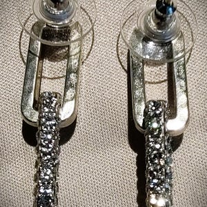 Pu&ograve; includere: Un paio di orecchini color argento con un design rettangolare pendente. La parte inferiore di ogni orecchino &egrave; incastonata con piccoli cristalli scintillanti. Gli orecchini hanno una chiusura a perno con un retro rotondo trasparente.
