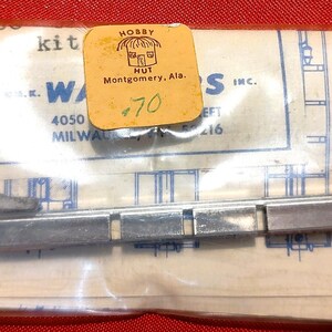 May include: A metal model kit component in a clear plastic bag with a yellow price tag reading .70. The kit includes a long, segmented silver metal bar, several smaller metal brackets, and two small gold-colored screws, all resting on a paper instruction sheet.