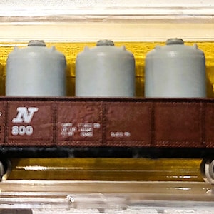 May include: A model train car with five gray cylindrical containers on a brown car. The car has the letters "L & N" and the number "28 800" printed on the side. The train car is in a clear plastic case with a yellow background.