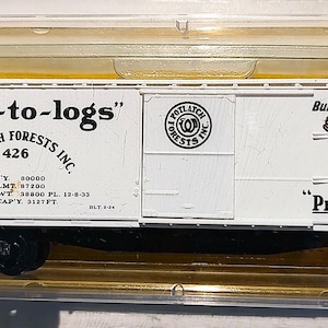 May include: A white model train car with black wheels and a black undercarriage. The car has the text "Pres-to-logs" and "Potlatch Forests Inc." printed on the side. The car is in a clear plastic case.