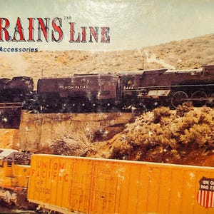May include: A product box for The Micro-Trains Line featuring a graphic of a black steam locomotive crossing a bridge above a yellow Union Pacific freight train. The text reads The Micro-Trains Line Authentic Scale Models and Accessories.