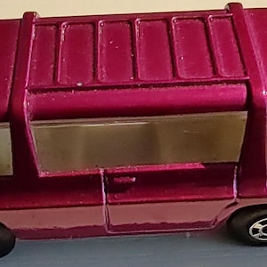 May include: A pink toy van with a white interior and black wheels. The van has a roof rack and a white windshield.