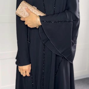 May include: A black abaya with a beaded trim. The abaya has a long, flowing silhouette and is made of a soft, comfortable fabric.