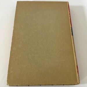 May include: A vintage book with a tan cover and a red, black, and blue spine. The cover shows signs of wear, with scratches and discoloration. The edges of the book are slightly worn, suggesting its age and use. The book's spine is visible, indicating the title and author.