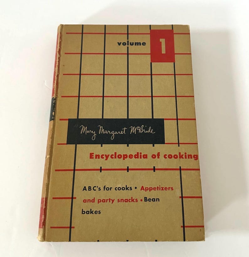 May include: A vintage cookbook titled "Encyclopedia of Cooking" by Mary Margaret McBride. The cover is tan with a red and black grid pattern. The book is labeled "Volume 1" in a red box. The book's contents include ABC's for cooks, appetizers, and bean bakes.