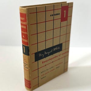 May include: Vintage cookbook, "Encyclopedia of Cooking, Volume 1" by Mary Margaret McBride. The book has a tan cover with a red and black grid pattern. The spine is red with white text. The title and author's name are visible.