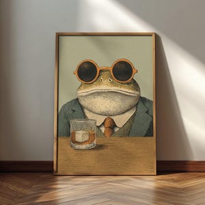 May include: Framed art print featuring a frog wearing orange sunglasses, a suit, and a tie, with a glass of whiskey. The artwork has a vintage, illustrated style, set against a light green background.