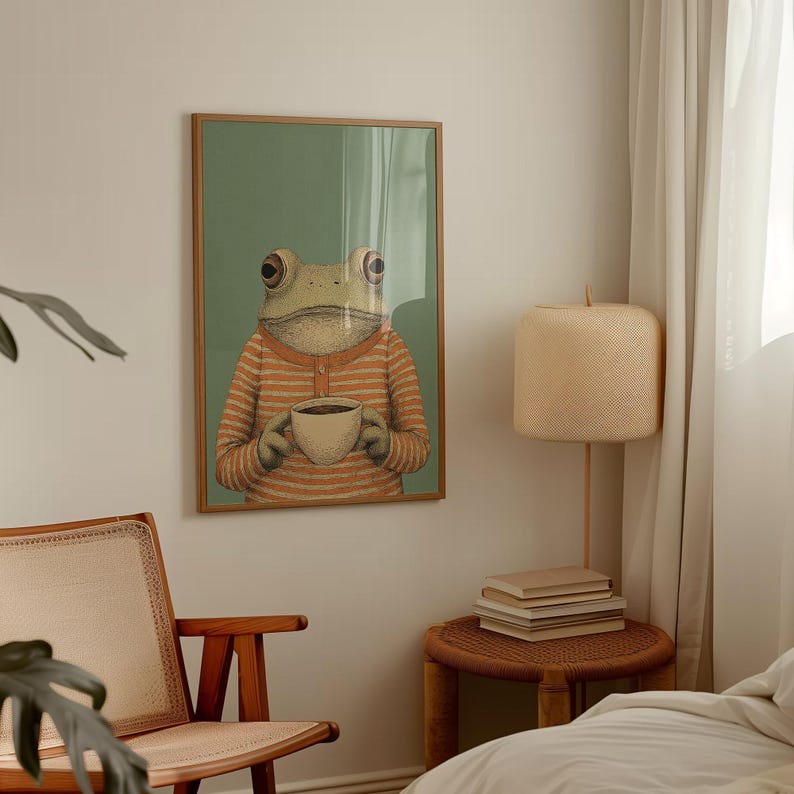 May include: A framed art print featuring a whimsical illustration of a frog wearing an orange and white striped shirt, holding a cup of coffee. The frog is set against a green background. The artwork is in a wooden frame.