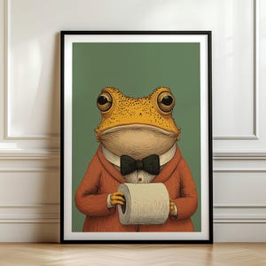 May include: Framed art print featuring a dapper frog in an orange suit and black bow tie, holding a roll of toilet paper. The frog has large, expressive eyes and is set against a green background. A whimsical and humorous piece.
