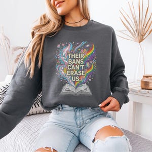 A woman wearing a gray sweatshirt with a colorful graphic design on it, sitting on a couch.