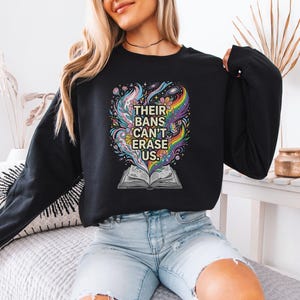 A woman wearing a black sweatshirt with a colorful graphic design on it, sitting on a couch.