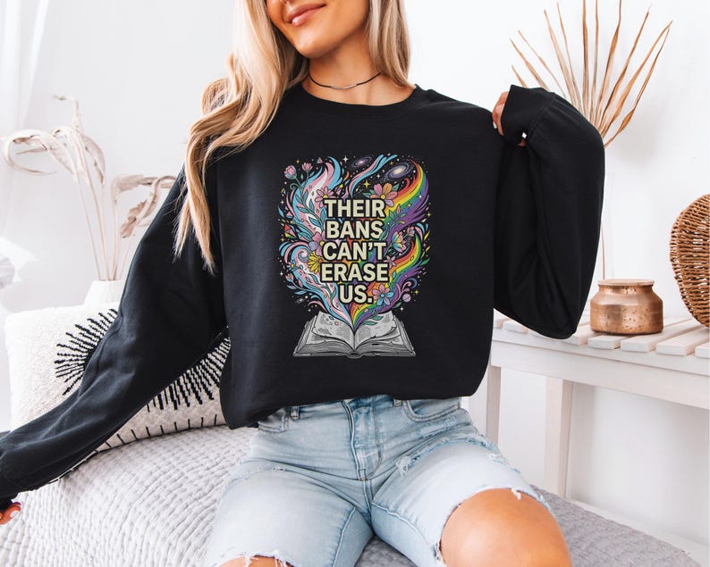 A woman wearing a black sweatshirt with a colorful graphic design on it, sitting on a couch.