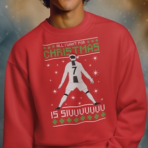 May include: Red Christmas sweater with a soccer player graphic. The sweater has the text "ALL I WANT FOR CHRISTMAS IS SIVUUUUUUU" in green and white. The soccer player is wearing a white uniform with the number 7.
