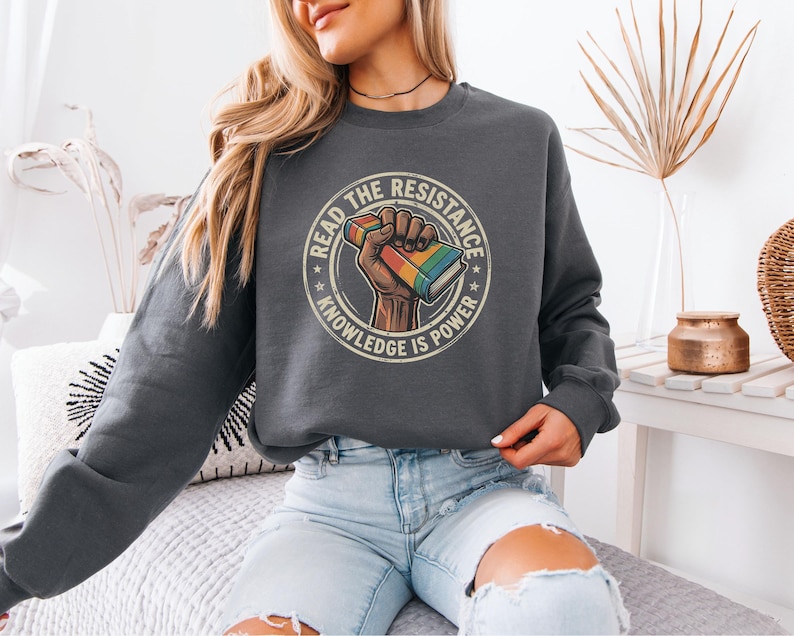 A woman wearing a gray sweatshirt with a graphic design on it, sitting on a couch.