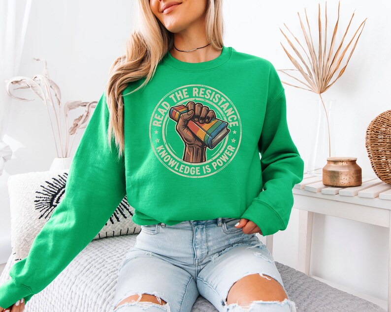 A woman wearing a green sweatshirt with a graphic design on it, sitting on a couch.