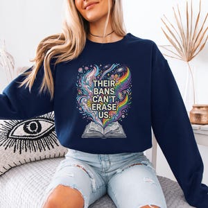 A woman wearing a navy blue sweatshirt with a colorful graphic design and text printed on it, sitting on a couch.