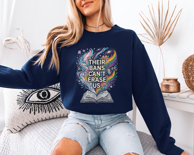 A woman wearing a navy blue sweatshirt with a colorful graphic design and text printed on it, sitting on a couch.