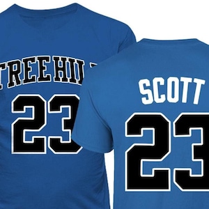 May include: Two royal blue t-shirts with black and white lettering. The front of one shirt says "TREE HOUSE" and the back of the other shirt says "SCOTT". Both shirts have the number "23" printed on them.