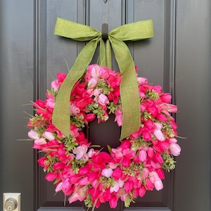 May include: A pink and white tulip wreath with a green bow hanging on a black door.