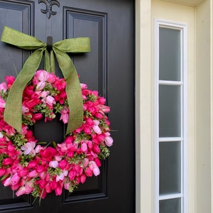 May include: A pink and green floral wreath with a green burlap bow hanging on a black door.