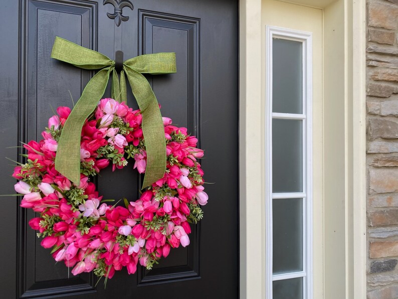 May include: A pink and green floral wreath with a green burlap bow hanging on a black door.