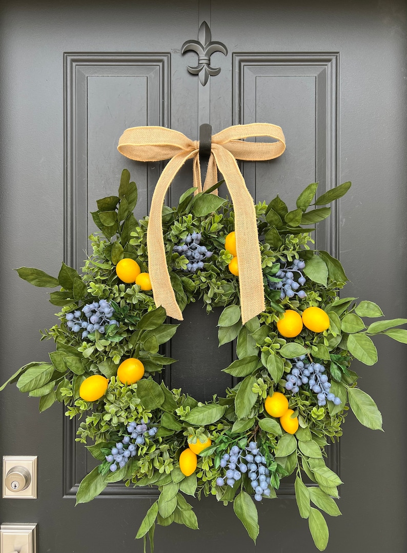 May include: A green wreath with yellow lemons and blue berries, decorated with a brown burlap bow, hanging on a black door.