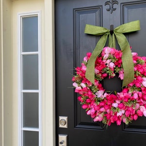 May include: A pink and green tulip wreath with a green burlap bow hanging on a black door.