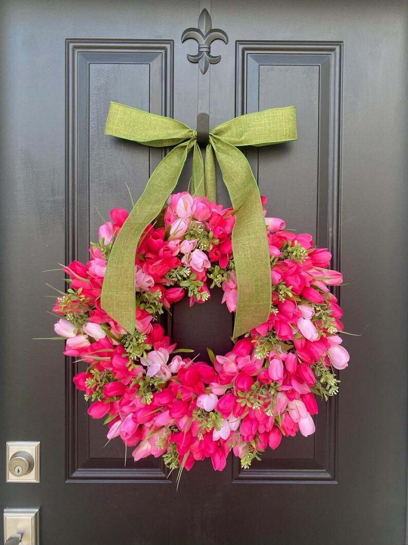 May include: A pink and white tulip wreath with a green bow hanging on a black door.