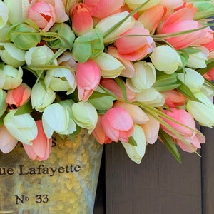 May include: A floral arrangement of artificial tulips in shades of pink, peach, and white, with green leaves. The flowers are in a galvanized metal bucket with the text "Rue Lafayette No. 33".