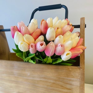 May include: A wooden box with a black metal handle filled with a bouquet of colorful tulips. The tulips are in shades of pink, peach, and white, with green leaves. The box has a natural wood finish.