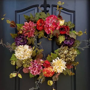 May include: A fall-themed wreath with a variety of flowers in shades of pink, red, yellow, and purple. The wreath is made with silk flowers and greenery and is perfect for decorating a front door.