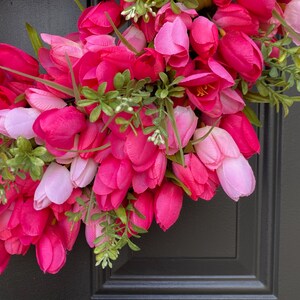 May include: A pink and white tulip wreath with green leaves. The wreath is made of artificial flowers and is perfect for spring decor.