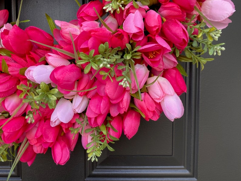 May include: A pink and white tulip wreath with green leaves. The wreath is made of artificial flowers and is perfect for spring decor.