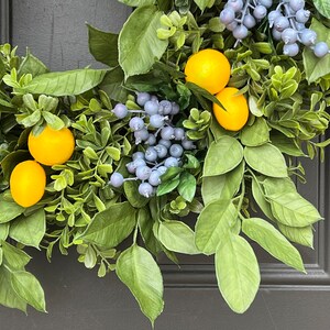 May include: A green wreath with yellow lemons and blue berries. The wreath is hanging on a gray door.