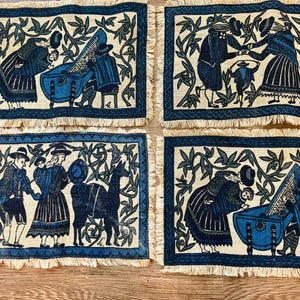 May include: Four rectangular placemats with a blue and cream folk art design. Each mat features a different scene with figures, animals, and musical instruments. The edges are trimmed with a blue border and a fringed edge.