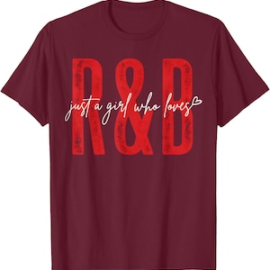 May include: A maroon short-sleeved t-shirt featuring large, distressed red letters R & B. Centered across the letters is the white cursive text "just a girl who loves" followed by a small white heart outline on the right side of the design.