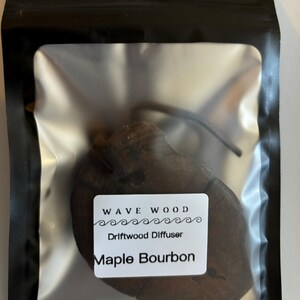 Puede incluir: Un difusor de madera flotante marrón en una bolsa de plástico transparente con una etiqueta blanca que dice "Wave Wood Driftwood Diffuser Maple Bourbon".