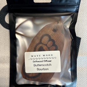 Op de afbeelding: Een bruine houten driftwood diffuser met een golfontwerp en de tekst "Wave Wood Driftwood Diffuser Butterscotch Bourbon".